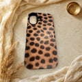 Warm tan cheetah print MagSafe case lying flat on cream linen and travertine stone