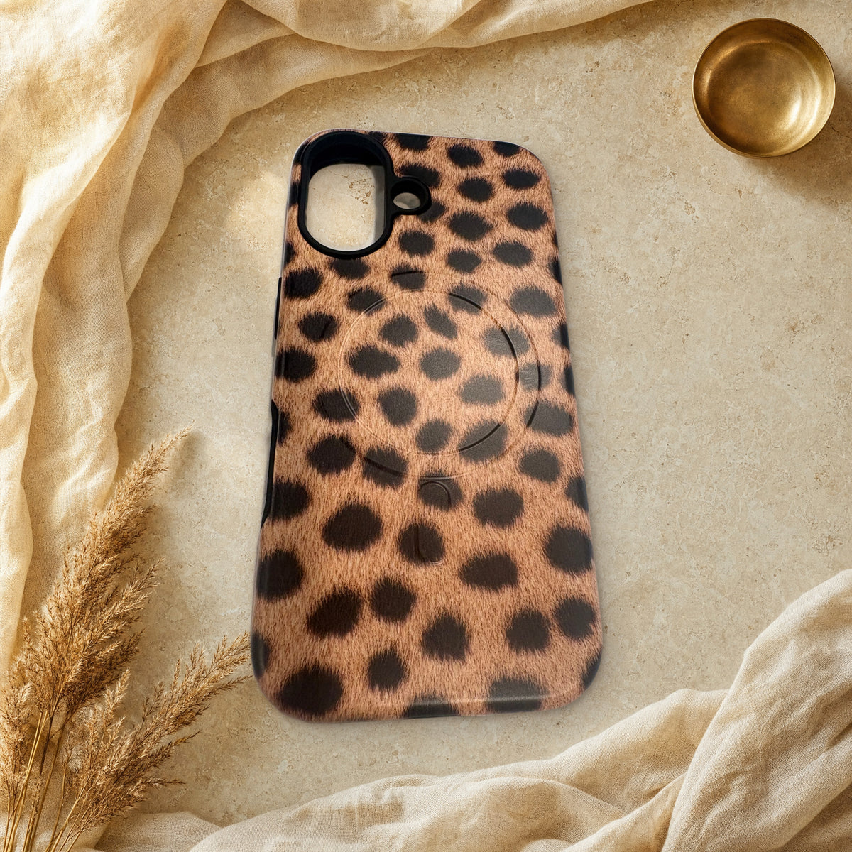 Warm tan cheetah print MagSafe case lying flat on cream linen and travertine stone