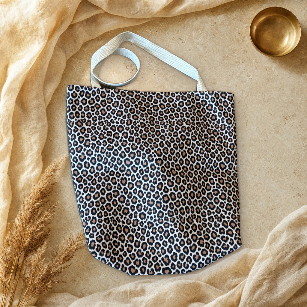 Classic cream leopard print canvas tote bag laid flat on cream linen and travertine stone